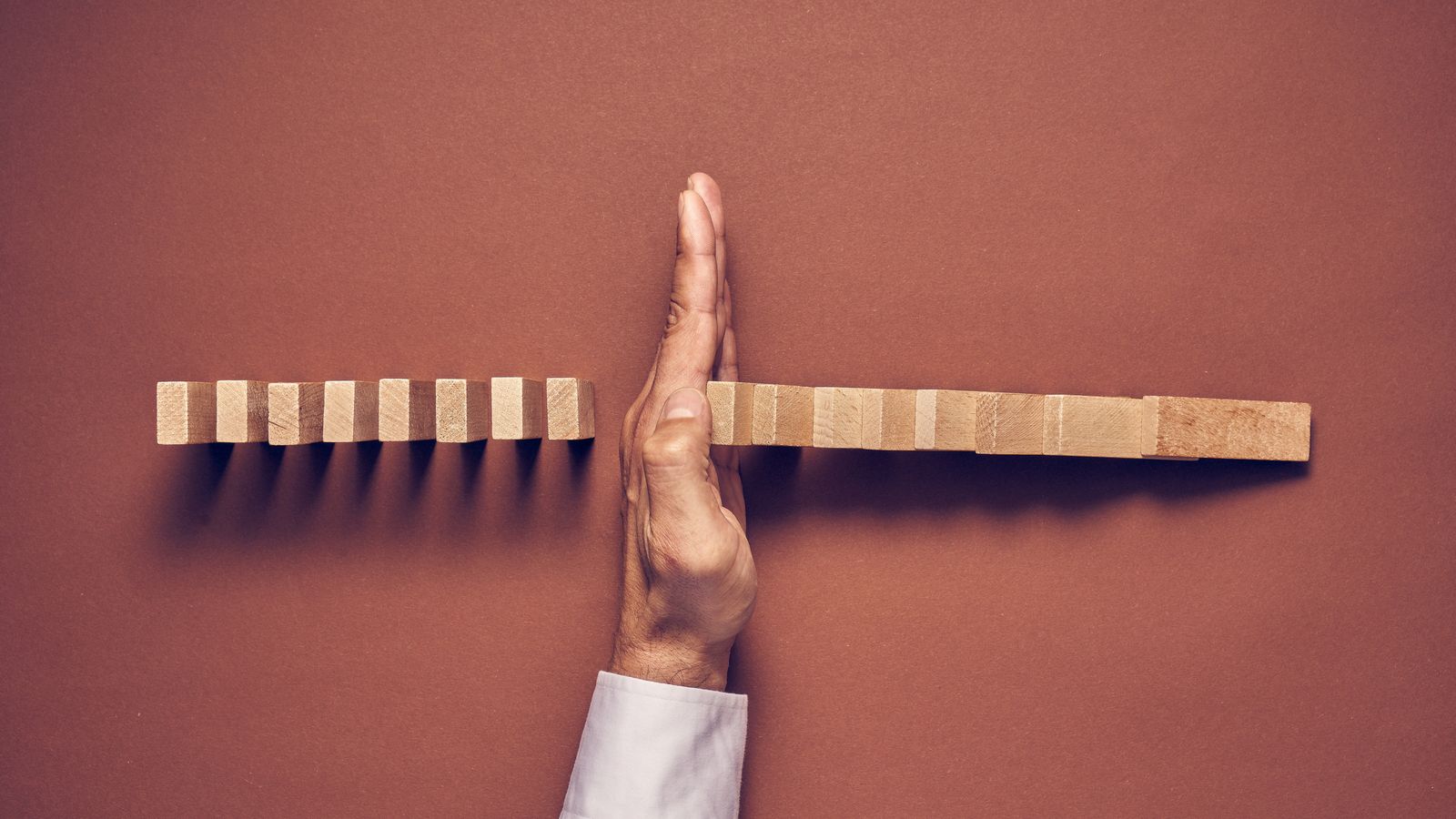A hand interrupts a row of wooden blocks, separating one section from the other against a brown background.